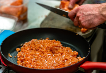 Red Pan with Pile of Cutted Salmon Pieces in the Foreground, Male Chef Cutting Fresh Salmon on the Wooden Board in the Background