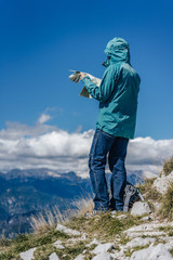 A woman on a hike looking into the map. Outdoor girl standing in the alpine mountain landscape exploring the map. A person with a map trekking and looking from a peak or summit.