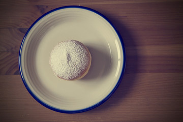 Vintage style overhead view of donut lying on ceramic plate on w