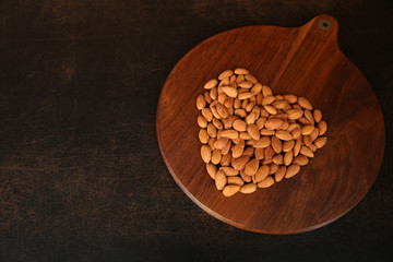 Sweet almond, folded in the form of a heart love on a brown wooden background with copy space for text. Healthy food. Flat lay. Top view. 
