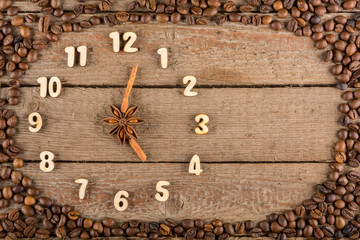 Decorative clock with wooden numerals and arrows made of cinnamon sticks, showing 5 o'clock, on a wooden background and a frame of coffee beans. Kitchen, advertising, banner, Copy space, flatly.