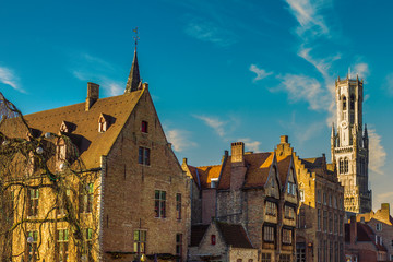 Fototapeta na wymiar Medieval buildings with brick walls, gabled roof and Belfry bell tower in background against a blue sky, sunny day for tourism in Bruges, province of West Flanders, Belgium