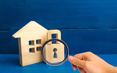 Magnifying glass is looking at the Wooden house with a padlock. House with a lock. Security and...