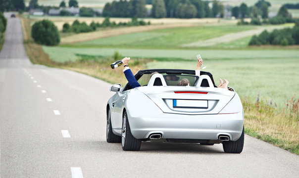 Newly wed couple driving a convertible car celebrating with champagne, Lithuania