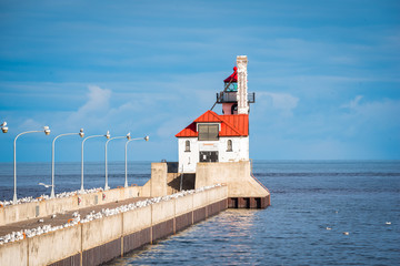 white light house, red roof out on pier, on a bright sunny blue sky day with wispy clouds.