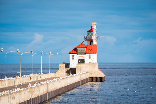 white light house, red roof out on pier, on a bright sunny blue sky day with wispy clouds.