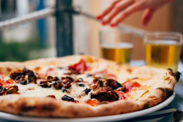 Close-up of an Aubergine pizza on a table and a woman's hand reaching for a beer