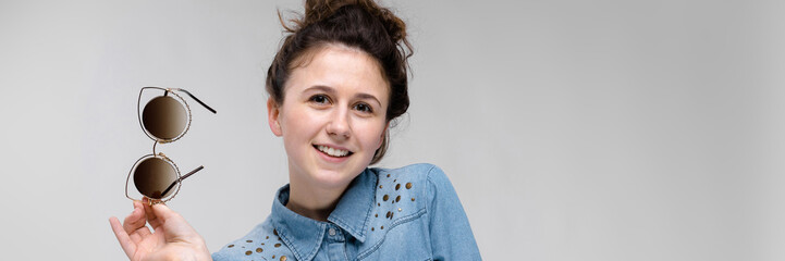 Young brunette girl holding glasses in her hand. Cat glasses. The hair is gathered in a bun.