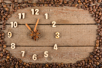 Decorative clock with wooden numerals and arrows made of cinnamon sticks, showing 11 o'clock, on a wooden background and a frame of coffee beans. Kitchen, advertising, banner, Copy space, flatly.