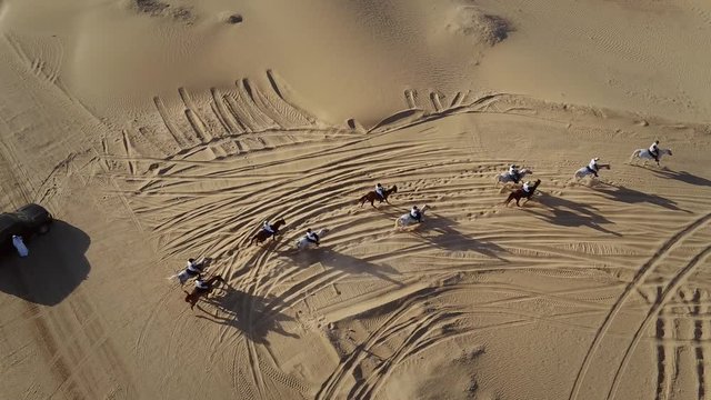 Aerial view group people riding horses on a race in the desert of Al Khatim in Abu Dhabi, U.A.E.