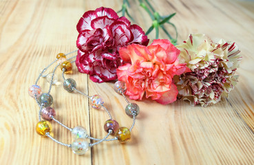Murano glass beads and a bouquet of carnations on a wooden table. Composition with flowers and handmade jewelry.