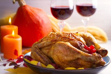 Chicken with fruits and berries on white table, decorated with autumn leaves, candles and pumpkin. Two glasses of red wine. Cozy atmosphere of autumn or thanksgiving dinner