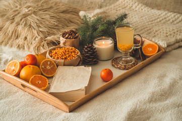 Soft cozy photo of woman in warm orange sweater on the bed with cup of tea and fruit. Girl sitting...