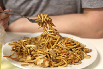 Unrecognizable person eating Chinese food, noodles with chicken and vegetables. Close-up, selective focus.
