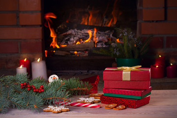 Christmas decorations, gifts and cookies on wooden table beside cosy open fire place. Winter holidays concept