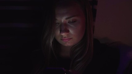 A woman looks at her phone in a dark room. Her face lit by only the glow of the screen as she is typing and reading. Cheating wife. Working late from home. Successful businesswoman concept. Close up. - Powered by Adobe