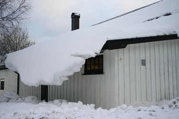 Snow overhangs from the roof of the house.