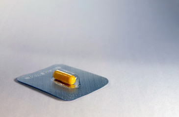 Yellow capsule pill in blister on white blue background with place for text.