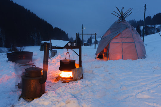 Old stove with tipi tent and alpine copper cheese making pot in the snow.