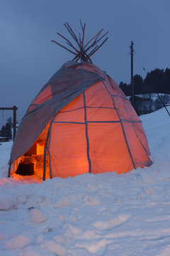 Tipi tent glowing from inside fire in the evening in snowy environment.