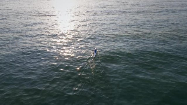 Aerial view above of a man paddling kayak in the sea at sunset.