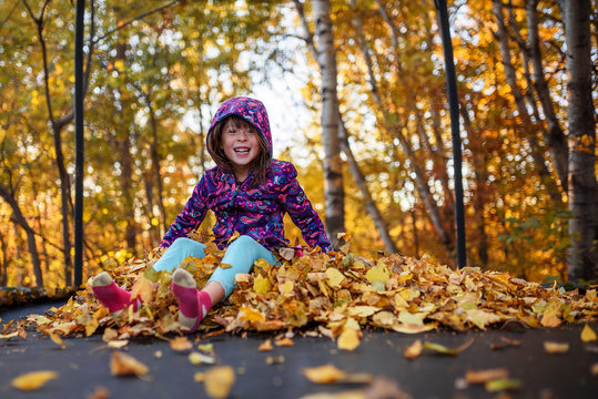 Smiling girl sitting on a stack of autumn leaves on a trampoline, United States