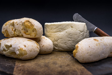 Cheese bread and brazilian minas white cheese on a wooden cutting board isolated in dark background