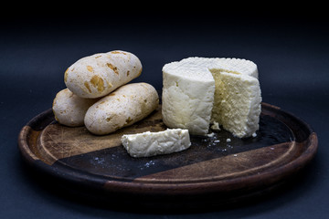 Cheese bread and brazilian minas white cheese on a wooden cutting board isolated in dark background