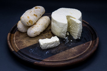 Cheese bread and brazilian minas white cheese on a wooden cutting board isolated in dark background