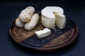 Cheese bread and brazilian minas white cheese on a wooden cutting board isolated in dark background