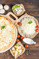Big cheese pizza on a round cutting board on a dark wooden background. Pizza ingredients