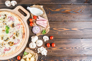 Food background design. Cream, cheese, ham, mushrooms, cherry tomatoes on a dark wooden background. Pizza Ingredients