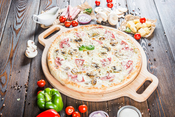 Creamy pizza with ham and mushrooms on a round cutting board on a dark wooden background. Pizza Ingredients