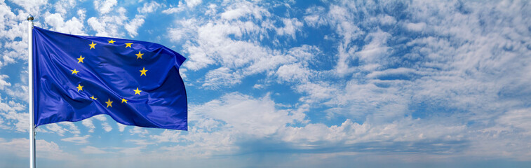Flag of the European Union waving in the wind on flagpole against the sky with clouds on sunny day, banner, close-up