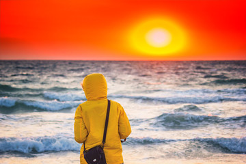 Beautiful sunrise above the stormy sea with girl in the hood looking into the distance, seascape