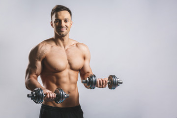 Muscular bodybuilder guy doing exercises with dumbbell over white background.