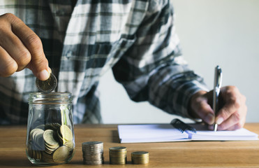 Business man putting coin in glass bottle saving bank and account for his money all in finance accounting concept.
