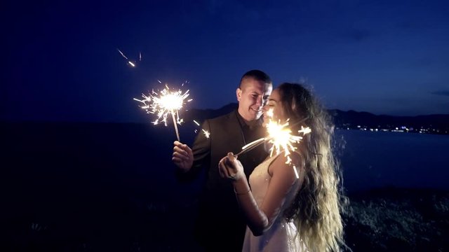 Cheerful newlywed couple holding big bright sparkling lights in the dusk, Crimea