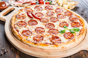 Large spicy pizza with salami and pepperoni sausage on a round cutting board on a dark wooden background. Pizza Ingredients. Macro
