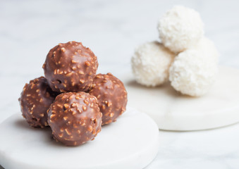 Luxury chocolate candies with hazelnuts and white cream with coconut flake round candies on marble coasters.