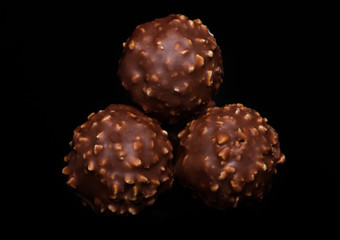 Luxury chocolate candies with hazelnuts and cocoa cream on black background.