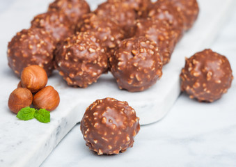 Luxury chocolate candies with hazelnuts pieces and mint leaf on marble board. © DenisMArt