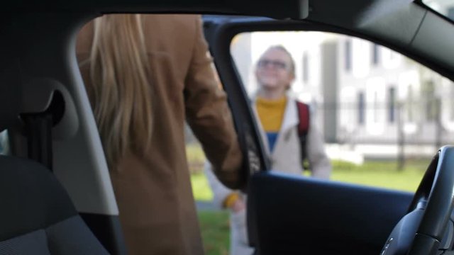 Gorgeous adult mother getting out of car and taking her teenage schoolgirl to school, walking hand in hand. Focus on vehicle interior. Blurry mom holding hands with daughter going to school.