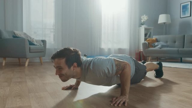 Muscular Athletic Fit Man in T-shirt and Shorts is Energetically Doing Push Up Exercises at Home in His Spacious and Bright Living Room with Modern Interior.