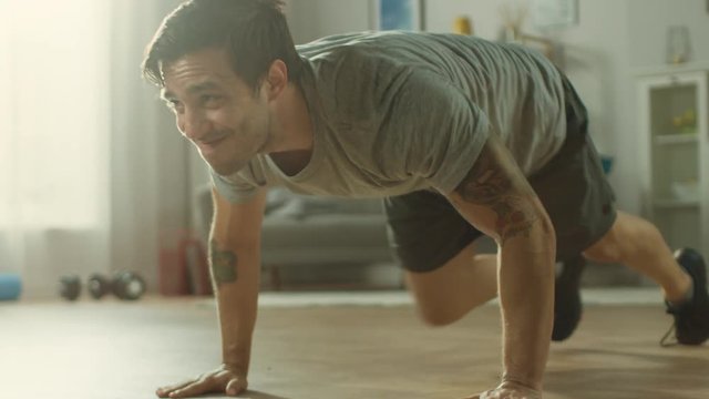 Slow Motion shot of a Muscular Fit Man in T-shirt and Shorts is Doing Mountain Climbers While Using a Stopwatch on His Phone. He is Training at Home in His Spacious and Bright Living Room.