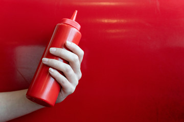 Hand holding a ketchup bottle on a red background in a diner