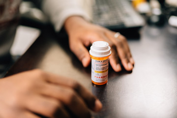 african american man taking opioid pills sitting at a dark table - obrazy, fototapety, plakaty