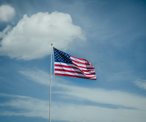 american flag waving in the wind against blue sky and big puffy clouds.