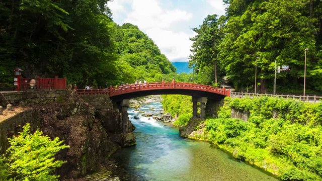 The beautiful emerald Daiya River flows under the red Unesco World Heritage Shinkyo Sacred Bridge, part of Futarasan Shrine on a crisp, blue sky day in Nikko, Japan. LR pan 4k time-lapse at 30fps