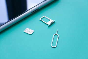 Closeup Shot of Sim Card, Eject Tool, and Tray on Turquoise Background